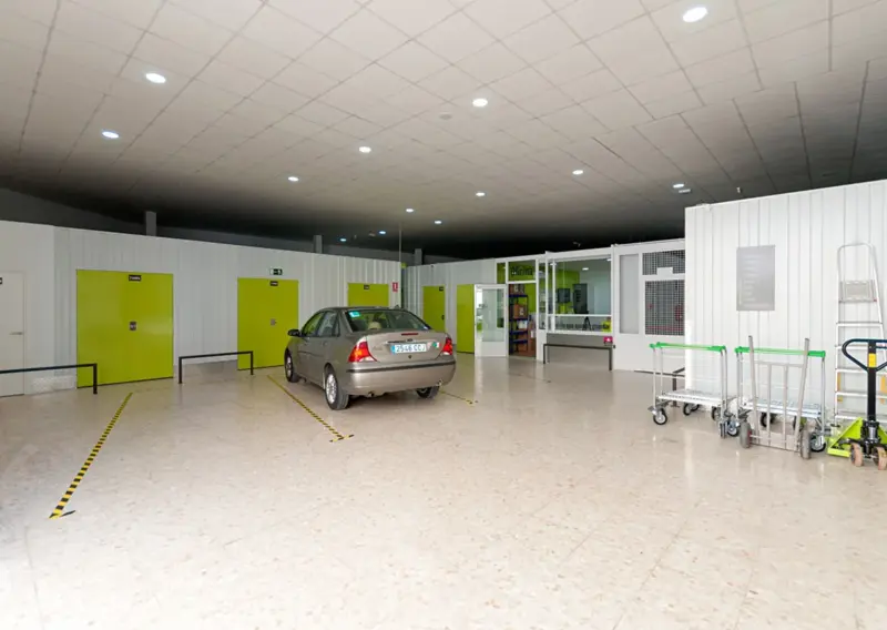 Zona interior de carga y descarga con un coche aparcado y carros de transporte en Keepy Ciudad Jardín, Málaga
