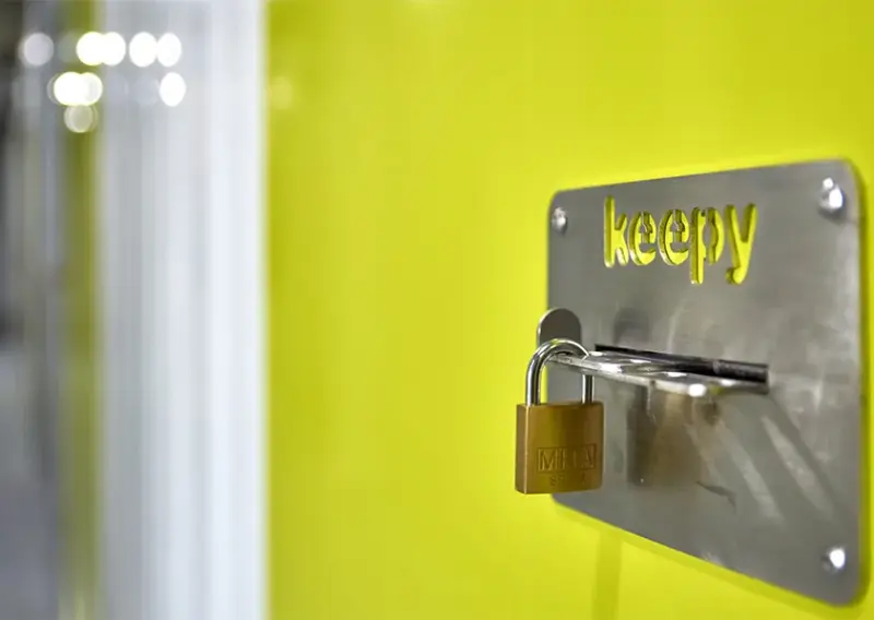 Candado cerrado sobre la placa Keepy de una puerta verde de trastero en La Huertecilla, Málaga