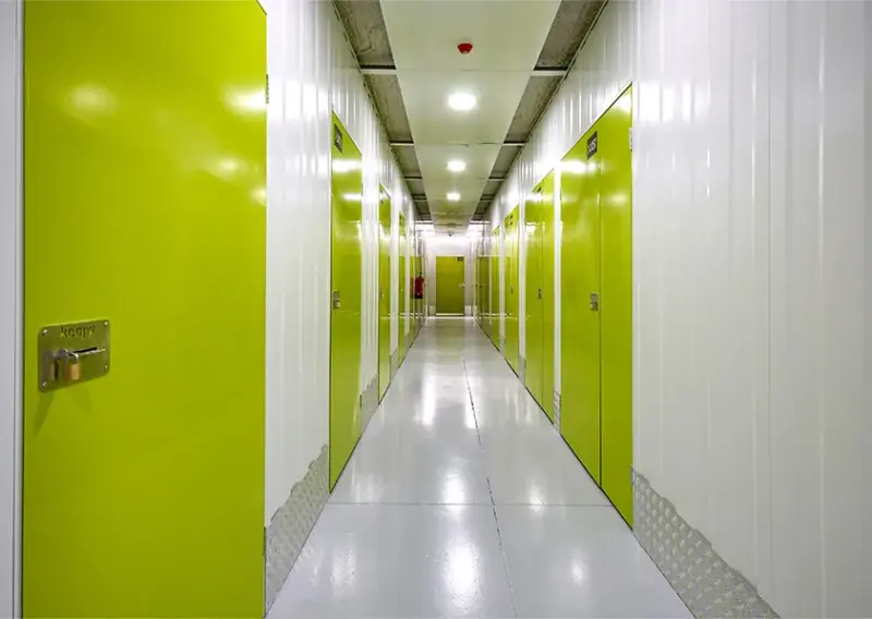 Pasillo de trasteros con puertas verdes y suelo claro en Keepy La Huertecilla, Málaga