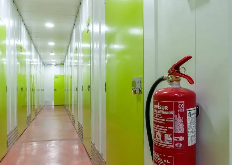 Extintor en la pared y pasillo de trasteros con suelo rojo en Keepy Marbella
