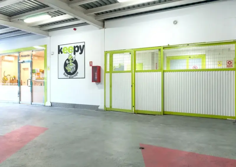Zona interior con cerramiento metálico verde y acceso a la recepción en Keepy Mijas