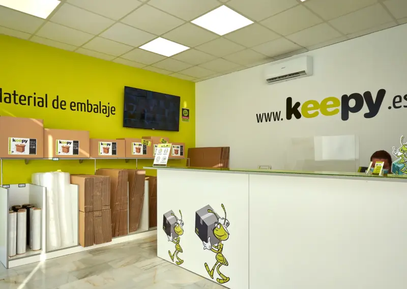 Recepción con mostrador blanco y pared de material de embalaje en el centro Keepy de Sevilla