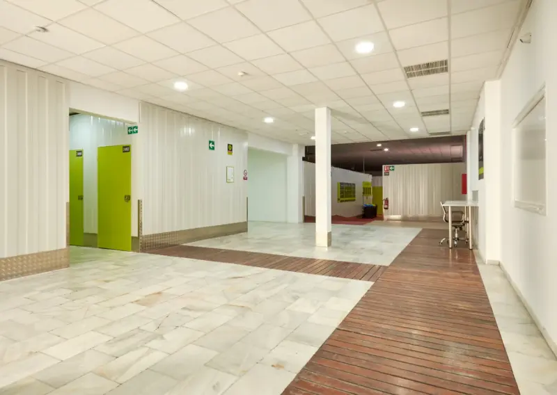 Zona diáfana con tarima de madera y puertas verdes de trastero en Keepy Sevilla