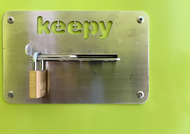 Candado cerrado sobre la placa Keepy de una puerta verde de trastero en Sevilla